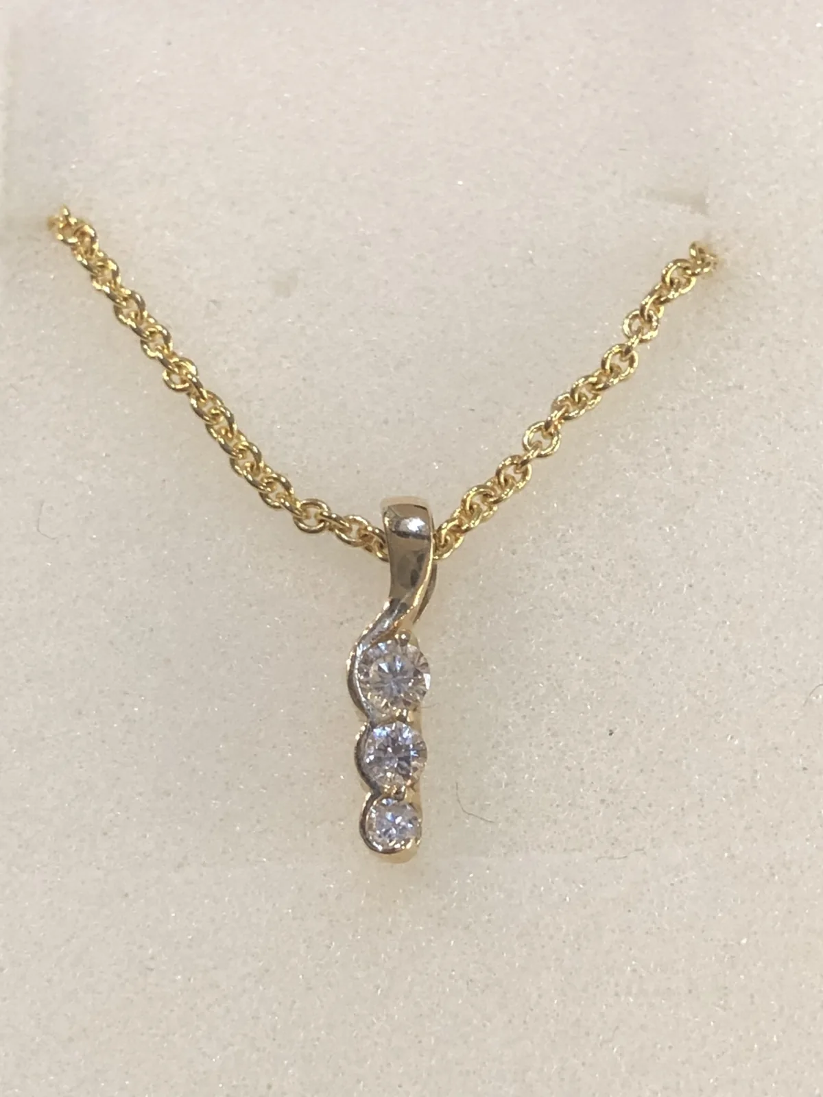 A three-stone diamond drop pendant on a yellow gold chain