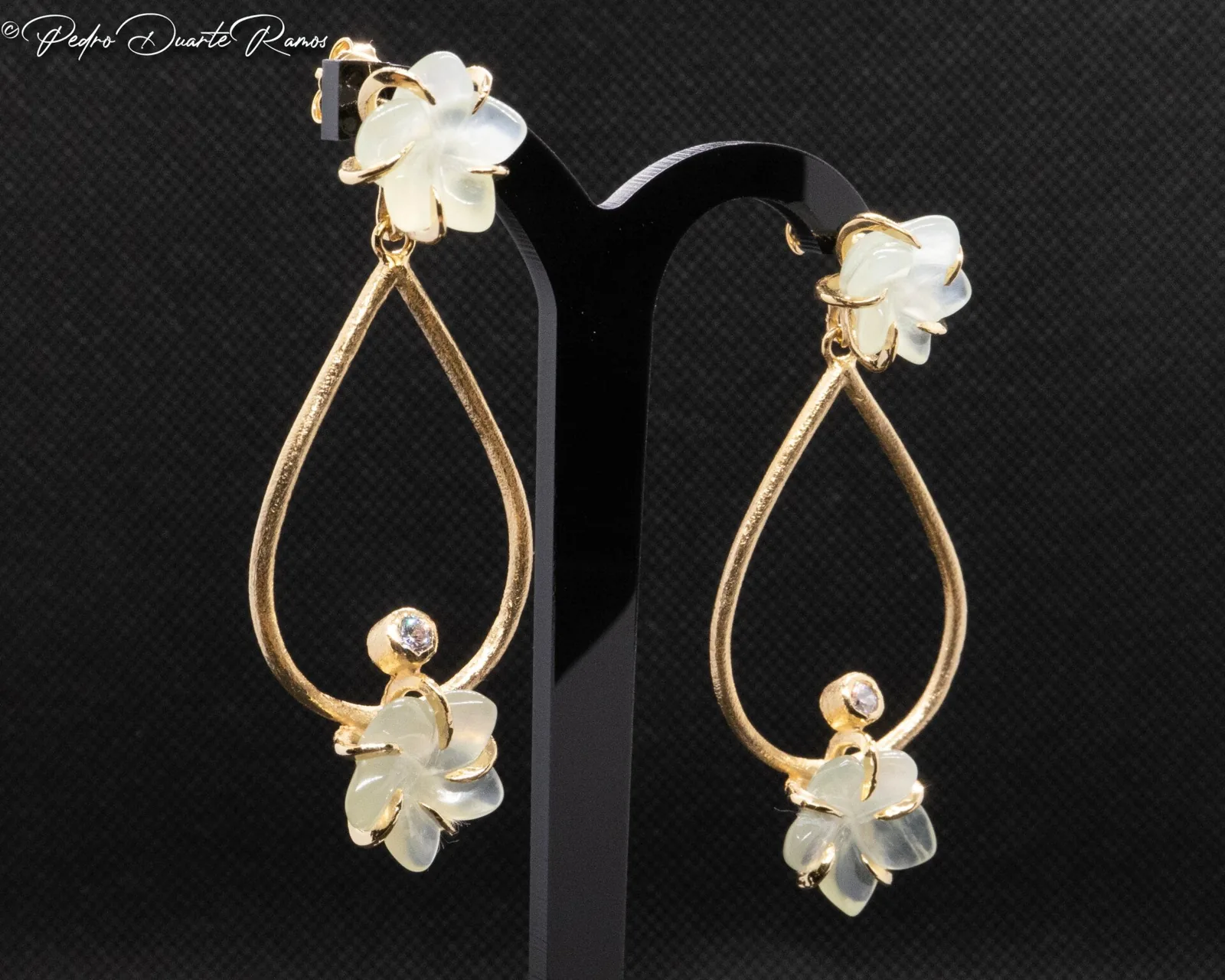 Gold teardrop earrings with small shell flowers, photographed on black