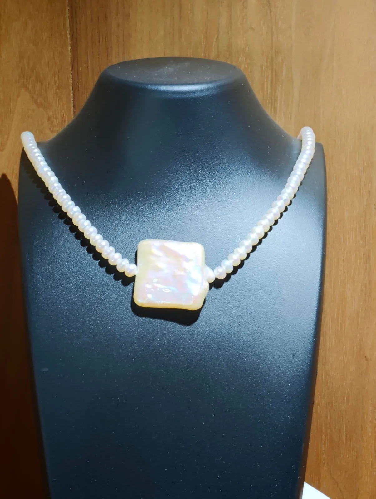 A pearl necklace with a square pendant on a display bust